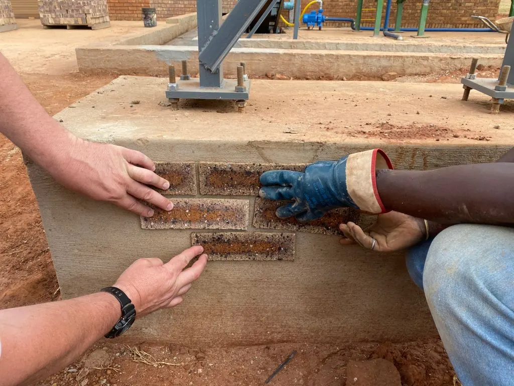 Hands placing brick tiles on a wall base